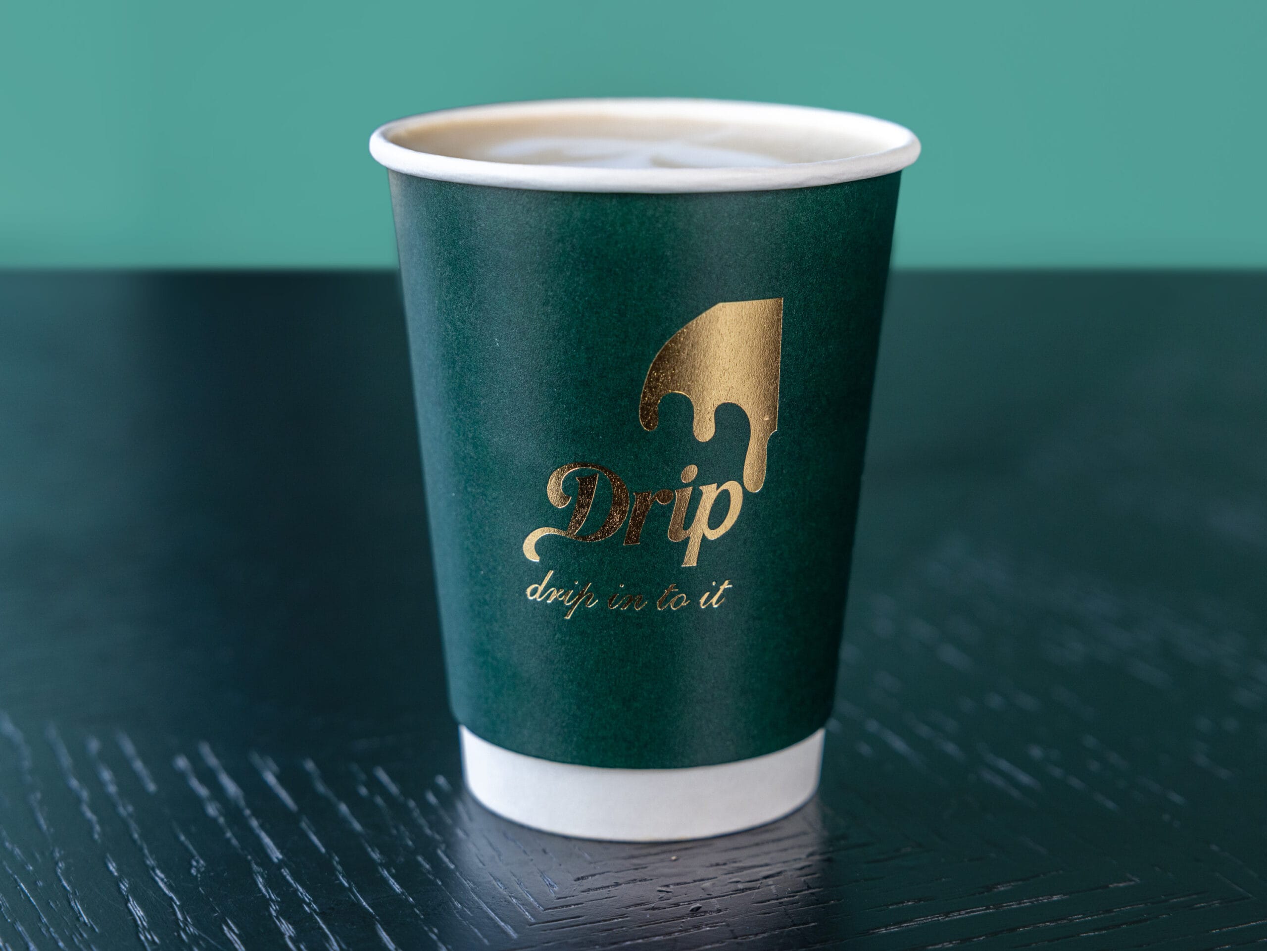 Drip Cafe hot Latte served in a signature dark green paper cup with a gold logo on a dark table.
