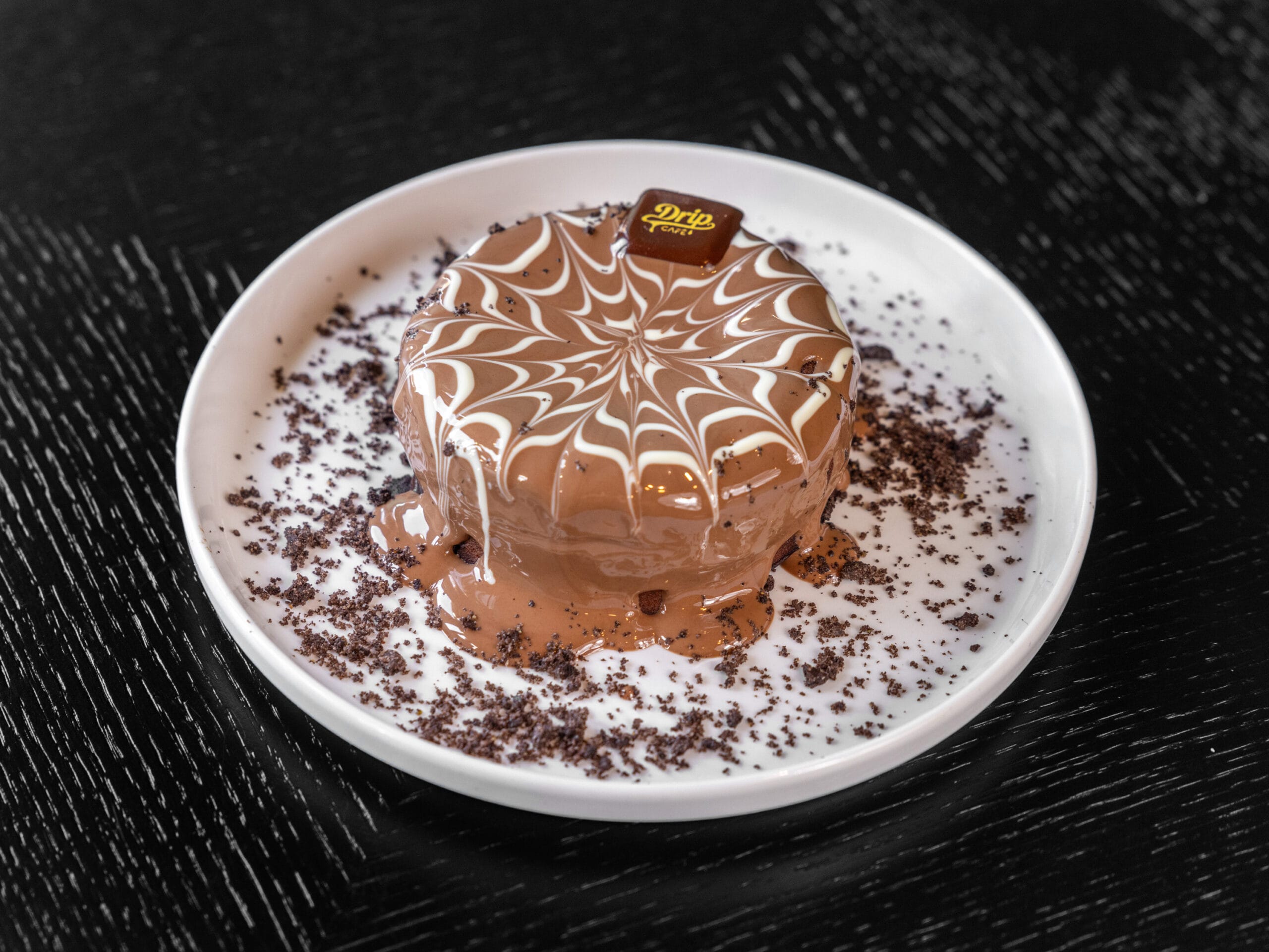 Drip Cafe Lava Cake, a single-serving chocolate cake coated in melted chocolate, topped with a white drizzle design, cookie crumbs, and a Drip Cafe chocolate piece.