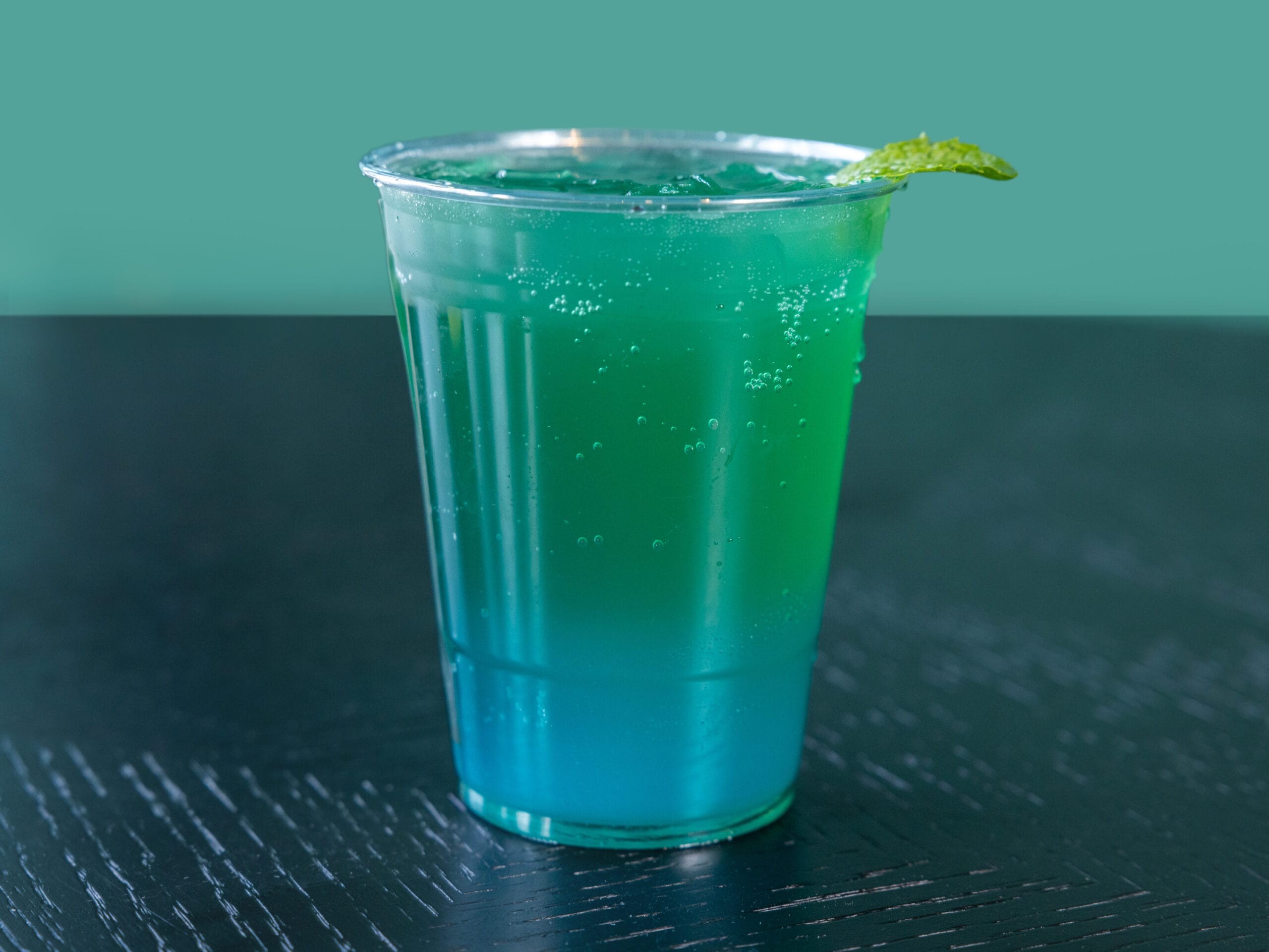 Drip Cafe Red Bull Mojito, a sparkling, layered drink with vibrant blue and green colors, served over ice and garnished with a mint leaf.