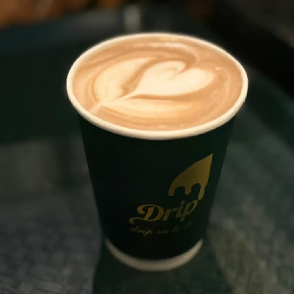 A rich mocha latte topped with smooth heart-shaped latte art, served in a dark green Drip cafe cup with gold logo detailing, featured as one of the indulgent Drip cafe menu items.