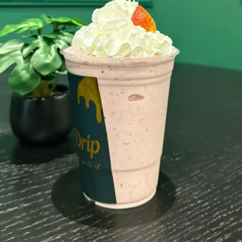 Drip Cafe Strawberry Shake, a creamy pink milkshake topped with generous whipped cream and a fresh strawberry slice